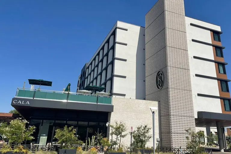 Contemporary hotel with white facade, decorative tower featuring textured panels, and Cala restaurant entrance with greenery