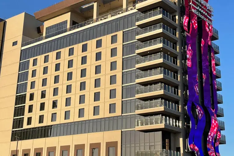 Modern high-rise with beige facade, glass balconies, and bright purple-pink LED display wrapping building corner