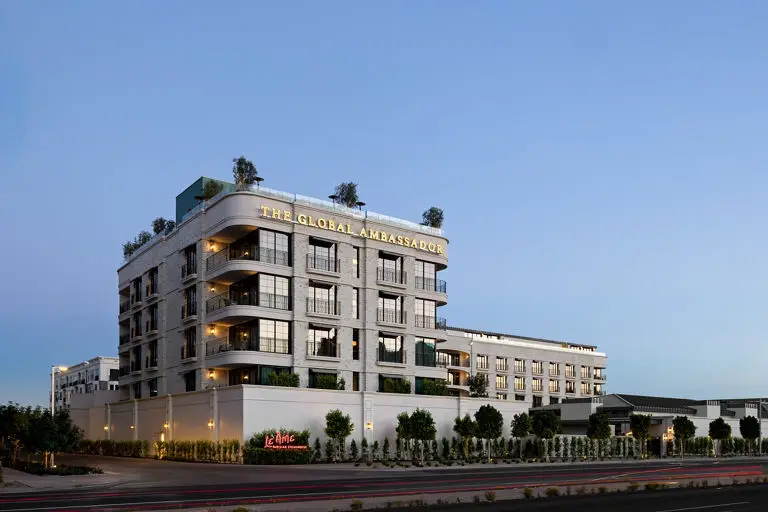 Modern Global Ambassador hotel building at dusk with white facade, rooftop greenery, and illuminated entrance signage