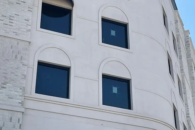 White modern building facade with arched window frames and dark tinted glass in geometric arrangement against blue sky