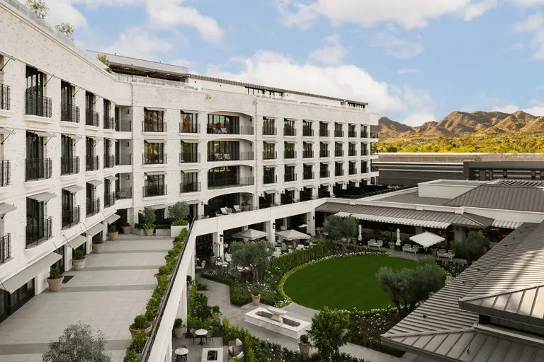 Luxury resort with white curved architecture, landscaped courtyard with green lawn, and desert mountains in background