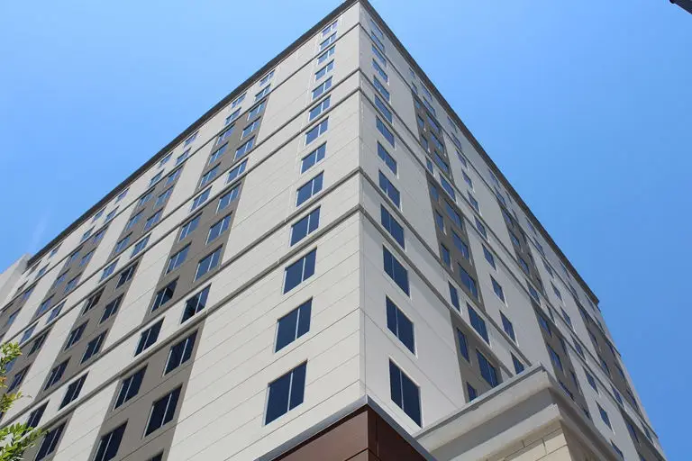 Modern multi-story residential building with beige facade and uniform windows photographed from below against blue sky